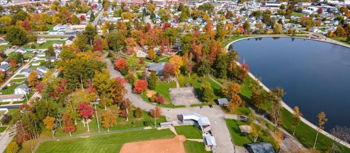 Aerial photography captures a bird's-eye view of a fall landscape, with a lake, tree, grass, field, and plant surrounded by water.